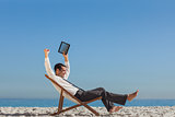 Victorious young businessman resting on his deck chair holding his tablet