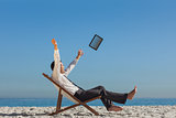 Victorious young businessman on his deck chair throwing his tablet away