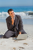 Smiling businessman sitting on the sand with his laptop