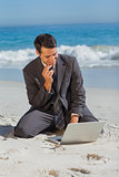Young businessman sitting on the sand with his laptop