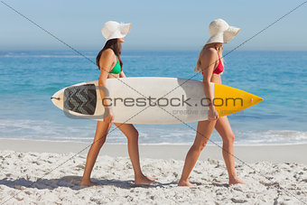 Two attractive women in bikinis holding a surfboard