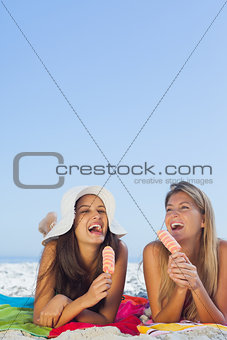 Smiling pretty women lying on their towel eating ice cream