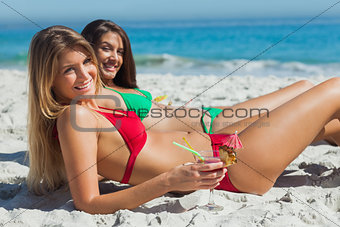 Cheerful tanned blonde and brunette taking sun drinking cocktails
