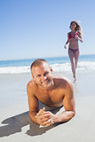 Smiling man lying on the sand while woman running to him