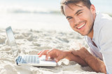 Smiling handsome man on the beach using his laptop