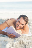 Smiling handsome man on the beach reading a book
