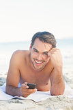 Smiling handsome man on the beach holding his cellphone