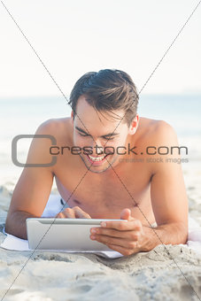 Handsome man lying on his towel using his tablet