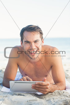 Smiling handsome man lying on his towel using his tablet