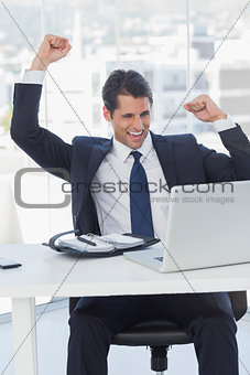 Businessman cheering and looking at his laptop