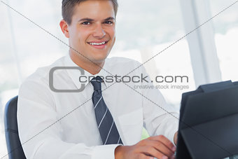 Smiling young businessman working on his tablet pc
