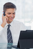Happy young businessman on the phone while working on his tablet