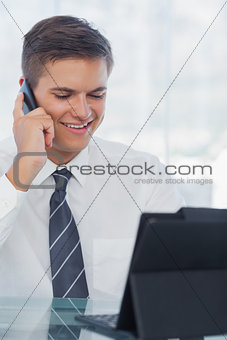 Happy young businessman on the phone while working on his tablet