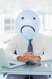 Blue balloon with sad face hiding businessmans face