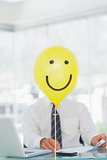 Yellow balloon with cheerful face hiding businessmans face