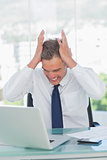 Angry businessman hands on his head looking at his laptop