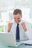 Victorious businessman cheering while looking at his laptop