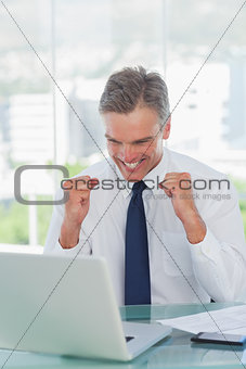 Victorious businessman cheering while looking at his laptop