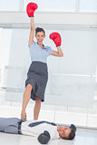 Businesswoman standing on defeated businessman wearing boxing gloves