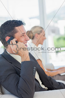 Cheerful businessman on the phone with his colleague working on computer