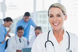 Cheerful blond doctor posing with colleagues in background