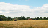 Red tractor baling straw in a farm field 