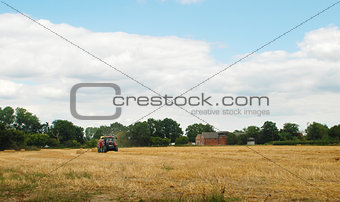 Red tractor baling straw in a farm field 