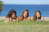 Group of three teenager girls typing on the mobile phone lying on the grass