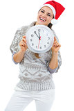 Smiling young woman in sweater and christmas hat showing clock