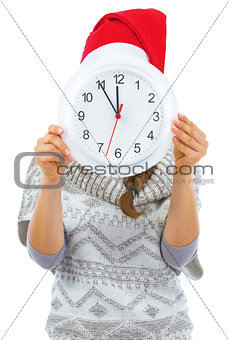 Young woman in sweater and christmas hat hiding behind clock