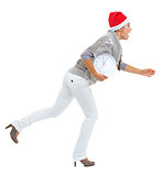 Shocked young woman in sweater and christmas hat running with cl