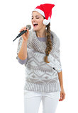 Happy young woman in sweater and christmas hat singing in microp