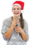 Smiling young woman in sweater and christmas hat with microphone