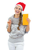 Thoughtful young woman in sweater and christmas hat holding lett