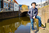 Cute teenage boy in hat (full-length portrait) against canal background