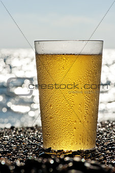 Plastic cup of beer standing on the sand by the sea.