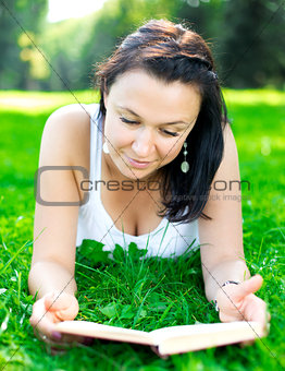 Beautiful girl lying on a grass with book
