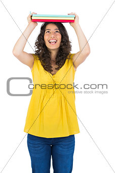 Cheerful curly haired student holding notebooks on her head