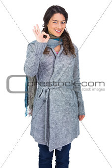 Smiling pretty brunette wearing winter clothes making ok gesture