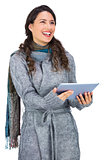 Happy brunette wearing winter clothes holding her tablet