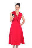 Smiling elegant brunette in red dress looking at her smartphone