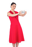 Smiling elegant brunette in red dress taking picture