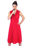 Content elegant brunette in red dress holding microphone