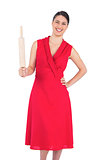 Smiling elegant brunette in red dress holding rolling pin