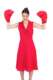 Serious gorgeous brunette in red dress wearing boxing gloves