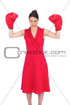 Serious gorgeous brunette in red dress wearing boxing gloves