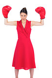 Unsmiling gorgeous brunette in red dress wearing boxing gloves