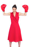Smiling gorgeous brunette in red dress wearing boxing gloves