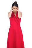 Glamorous model in red dress covering her ears