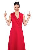Smiling glamorous model in red dress pointing up